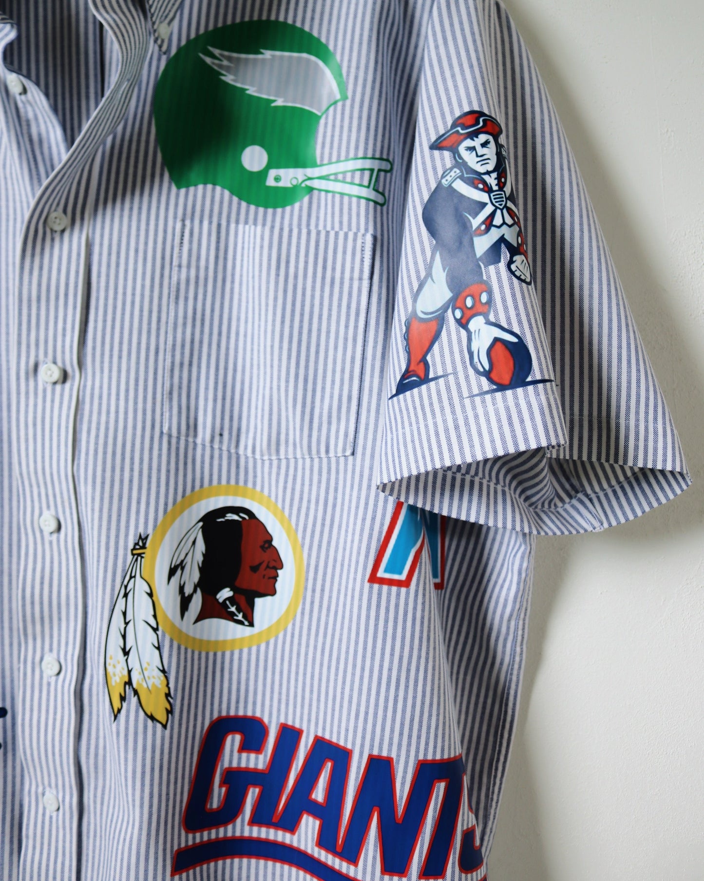 Striped shirt with sports team logos and graphics on a plain background