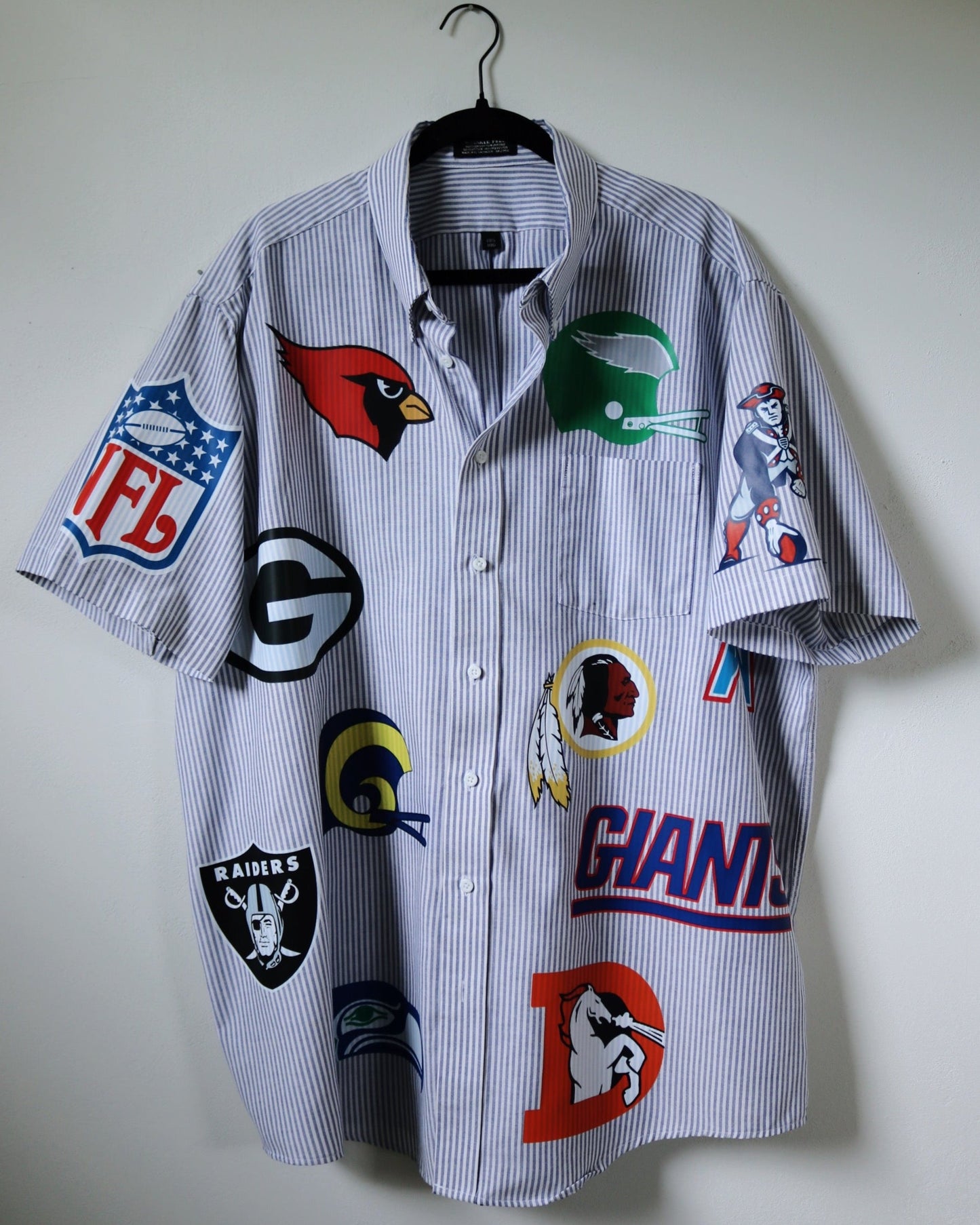 Shirt with sports team logos on a hanger against a plain background