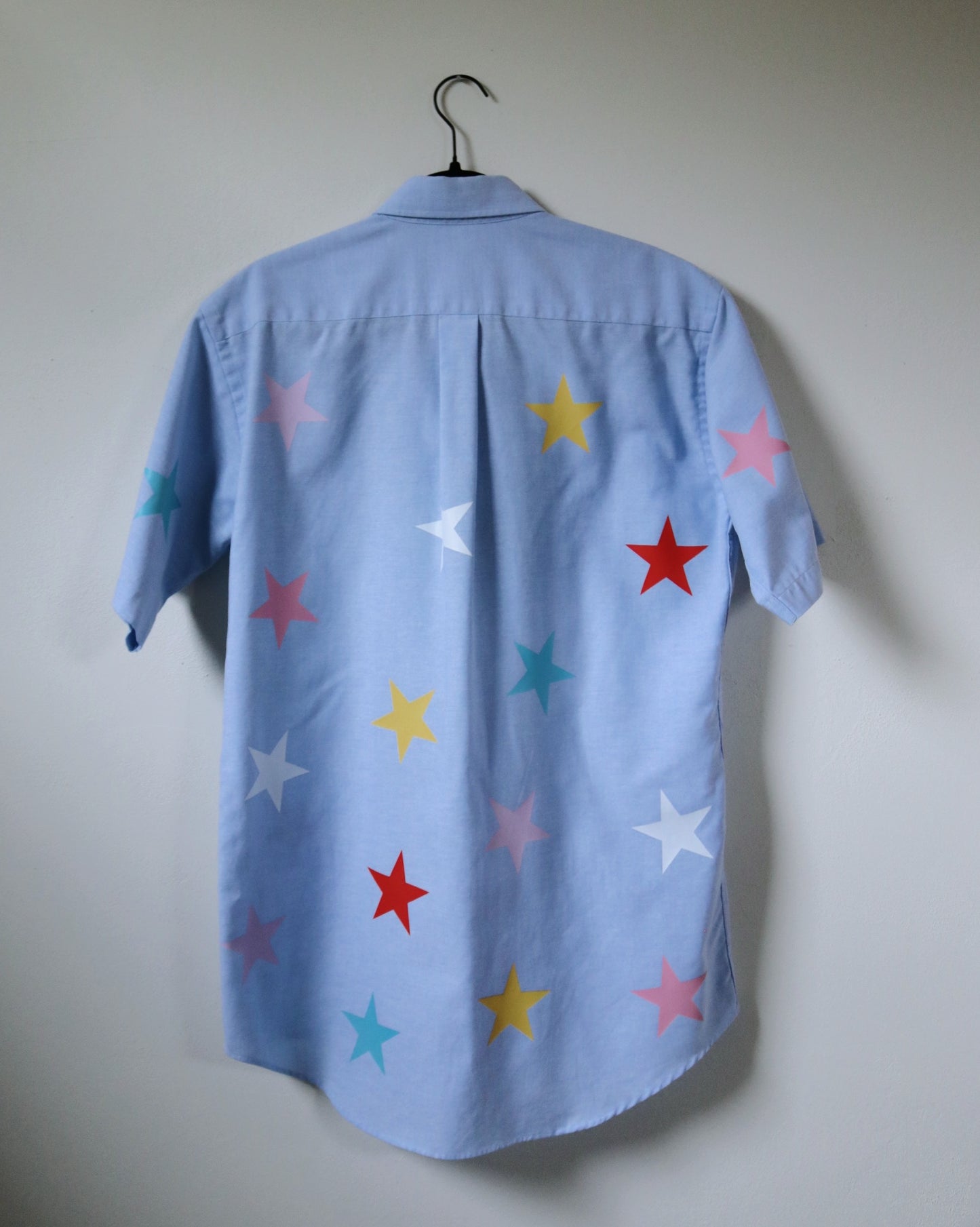 Light blue shirt with colorful star patterns on a white wall