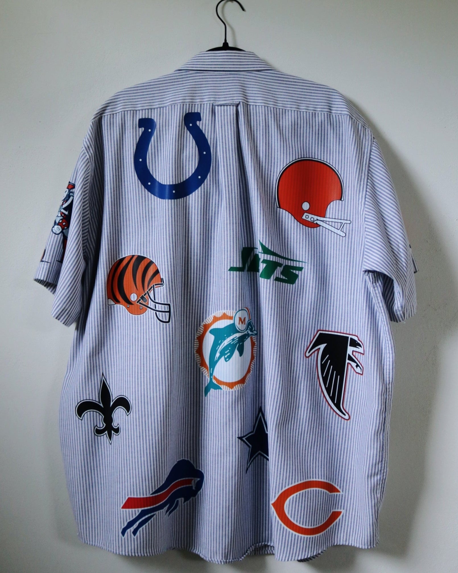 Shirt with various sports team logos on a hanger against a plain wall