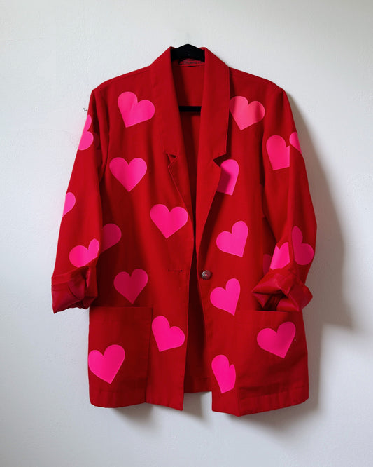 A red blazer with a pattern of neon pink hearts spread across the fabric, displayed against a white background. Upcycled womens jacket with bold neon pink hearts.