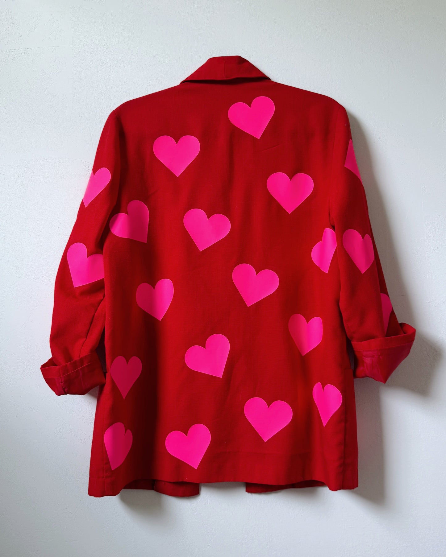 Upcycled red blazer with neon pink hearts, back view, hanging on wall, bold one-of-a-kind jacket