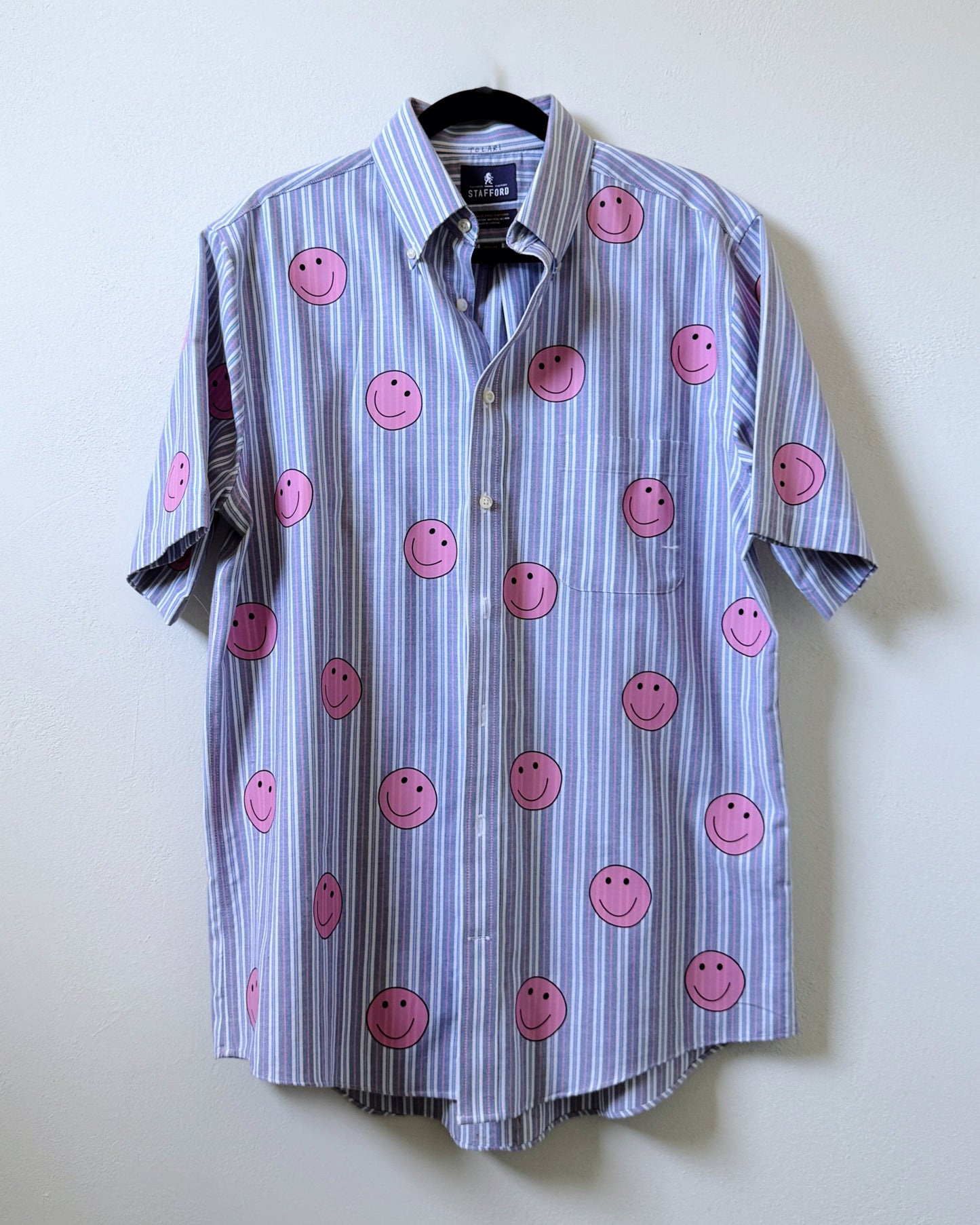 A button-up shirt with a striped pattern featuring pink smiley face designs on the front.