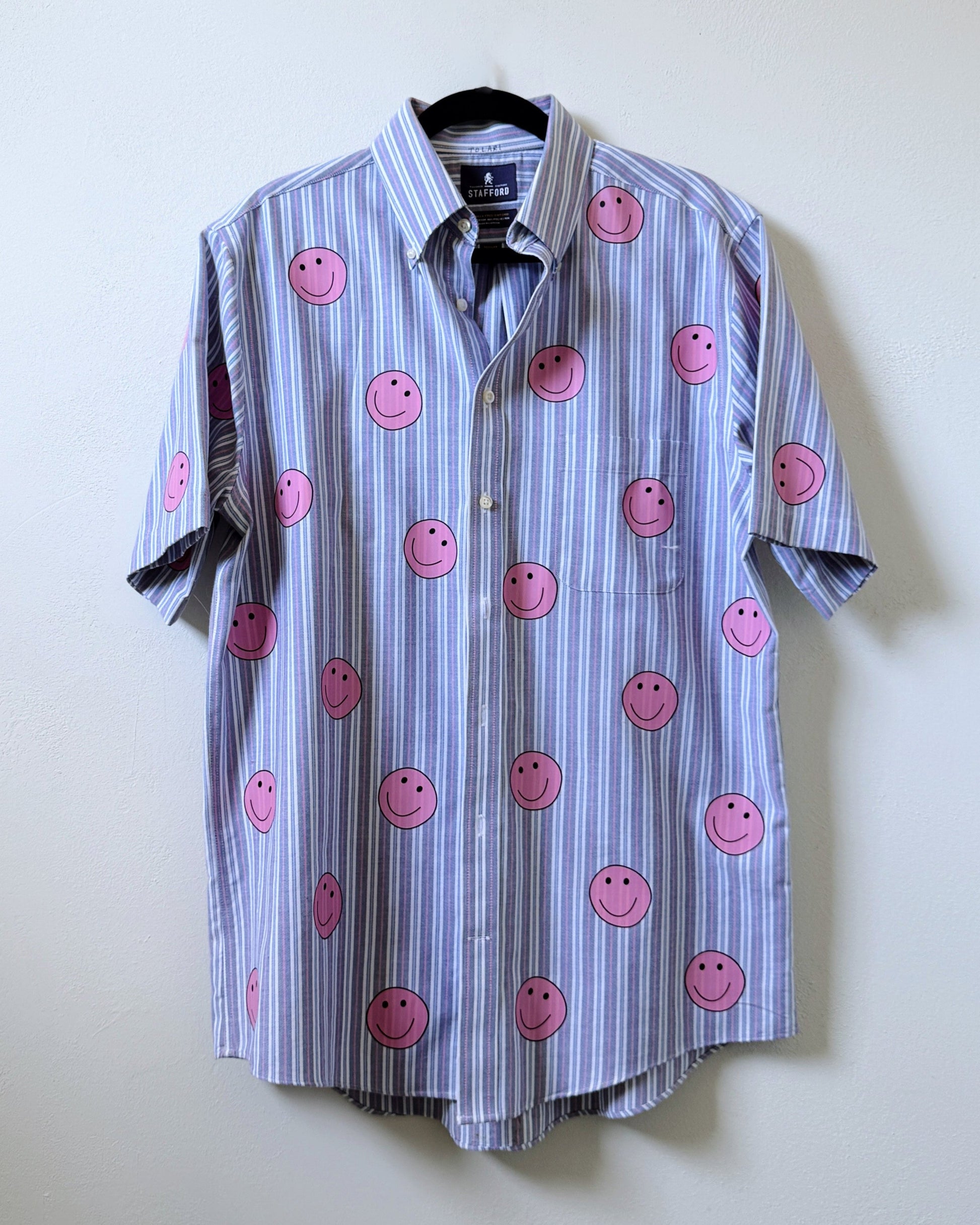 A button-up shirt with a striped pattern featuring pink smiley face designs on the front.