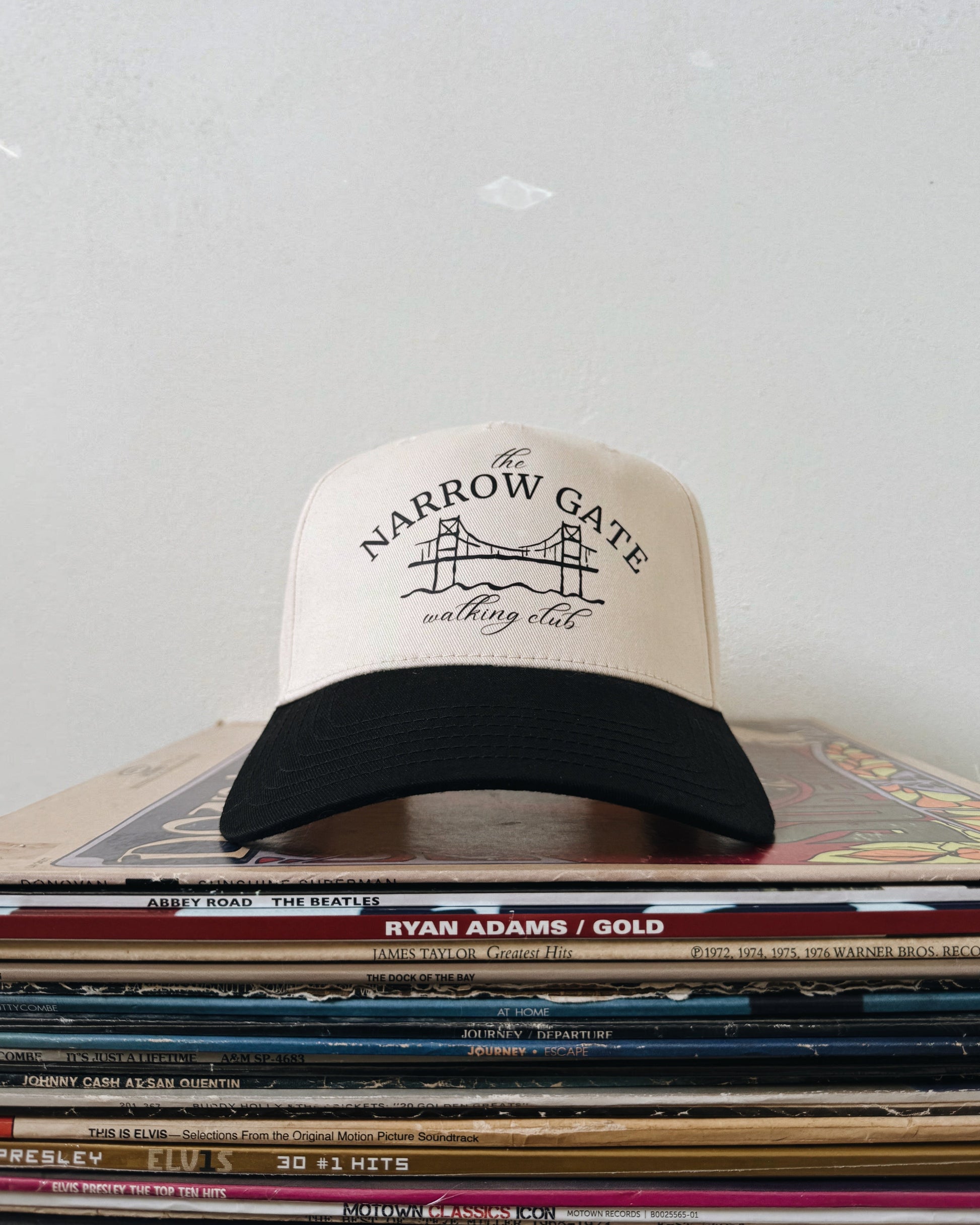 A beige and black baseball hat with text on the front, placed on a stack of vinyl records.
