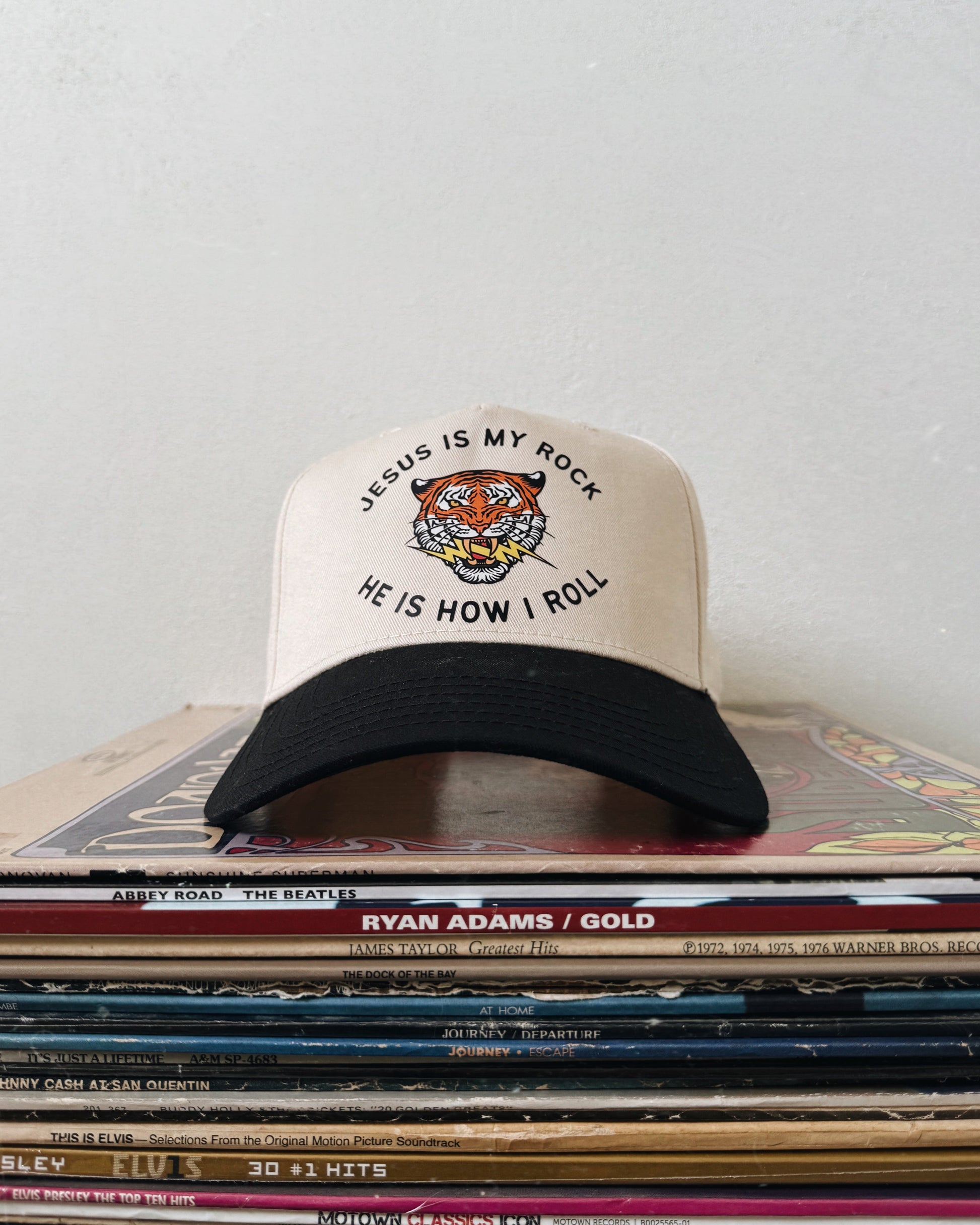 A beige and black baseball hat with text on the front, placed on a stack of various items.