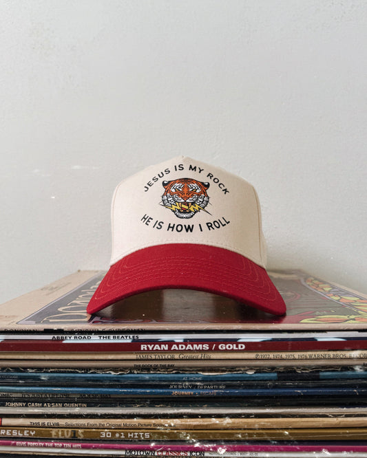 A beige and red baseball hat with text on the front, placed on a stack of various items.