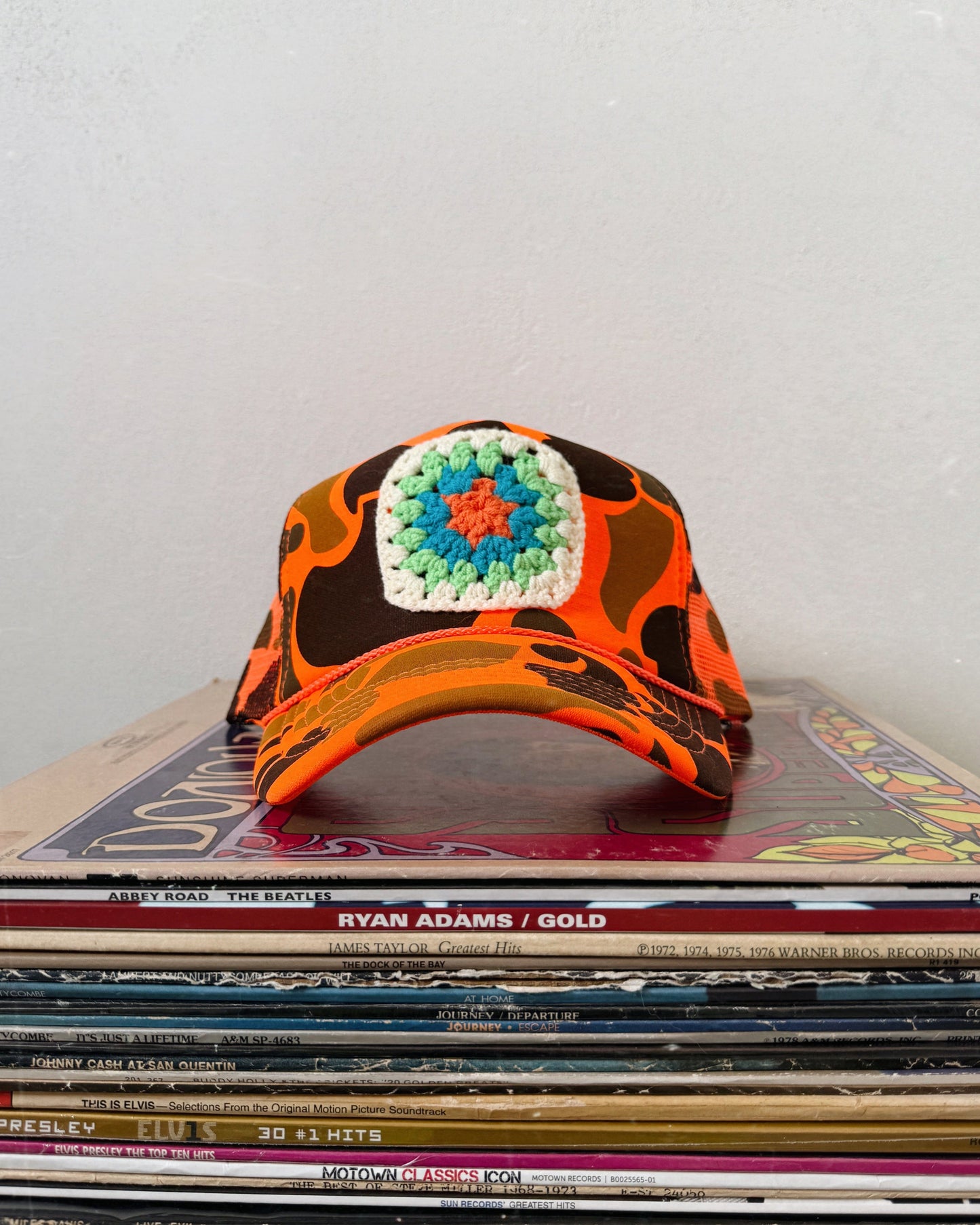 A multicolored trucker hat with a geometric pattern, placed on a stack of old vinyl records. Custom granny square trucker hat for women boho style