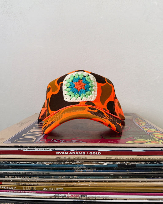 A multicolored trucker hat with a geometric pattern, placed on a stack of old vinyl records. Custom granny square trucker hat for women boho style