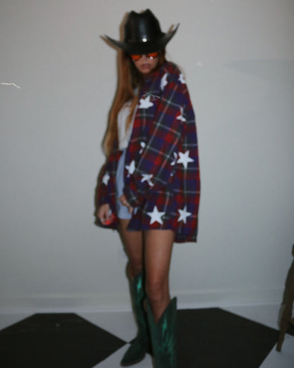 Person wearing a plaid coat with star patterns, green boots, and a black cowboy hat indoors.