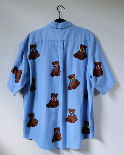 Blue shirt with brown teddy bear patterns on a hanger against a white wall