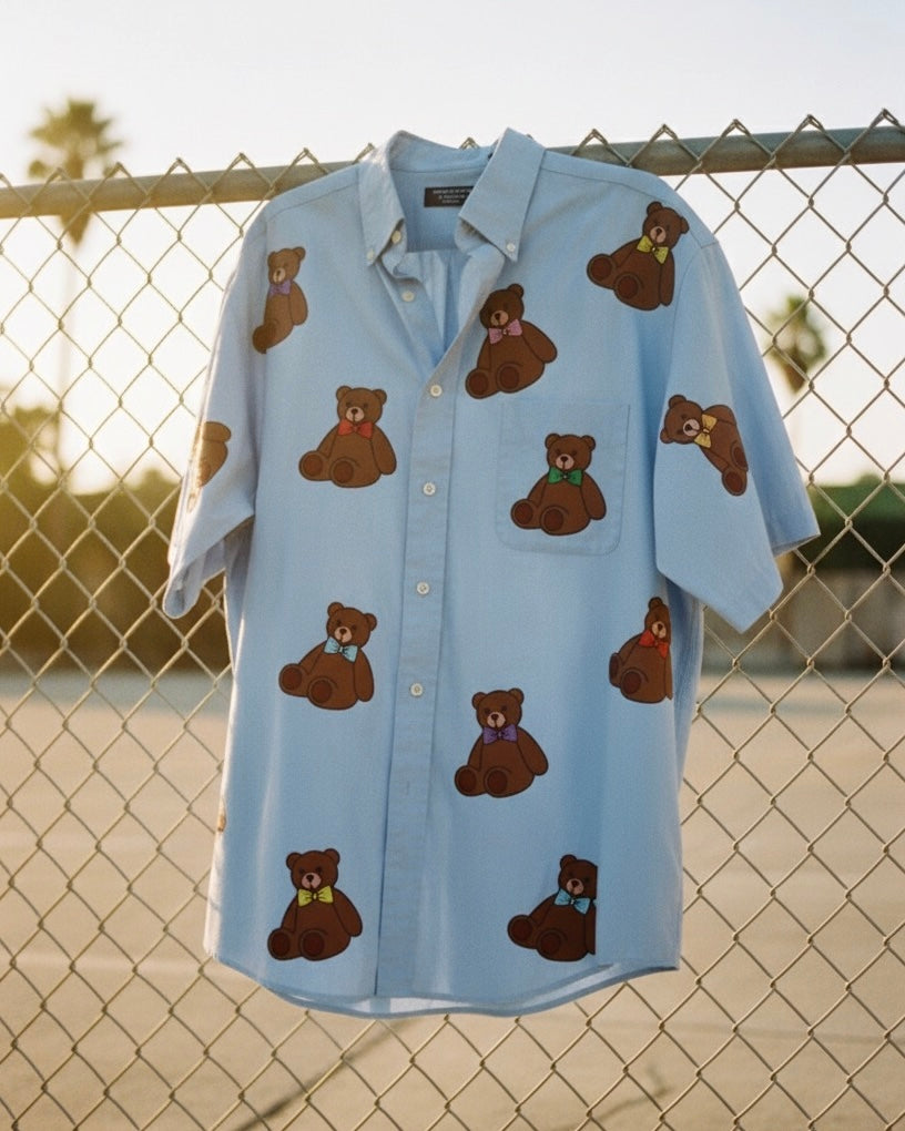 Light blue shirt with brown teddy bear patterns hanging on a chain-link fence.