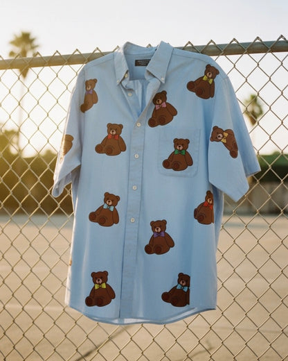 Light blue shirt with brown teddy bear patterns hanging on a chain-link fence.
