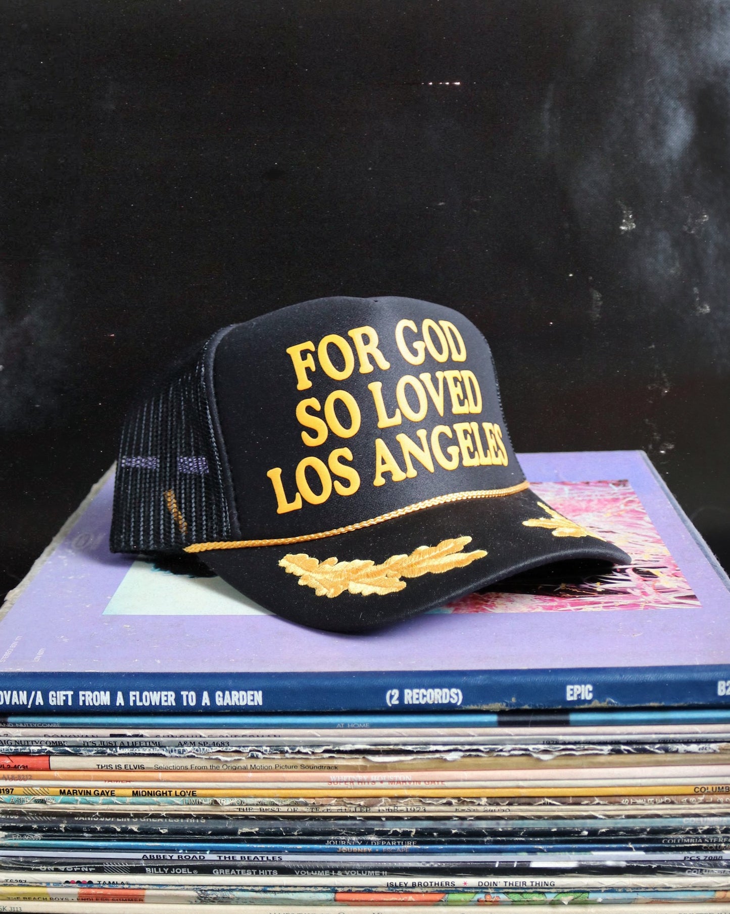 Black cap with 'For God So Loved Los Angeles' text on a stack of records