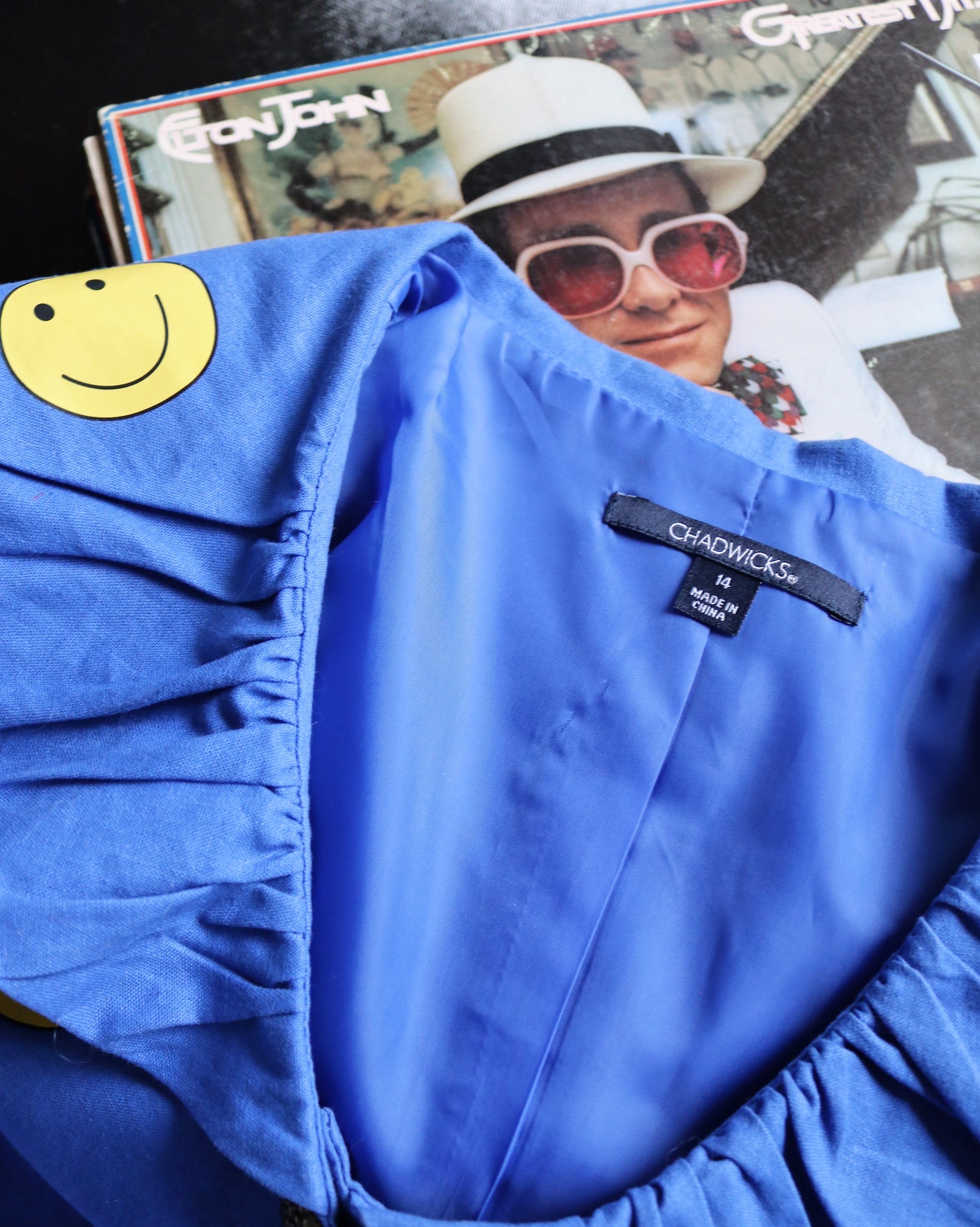 Blue jacket with a smiley face patch and a magazine featuring a person in sunglasses in the background.
