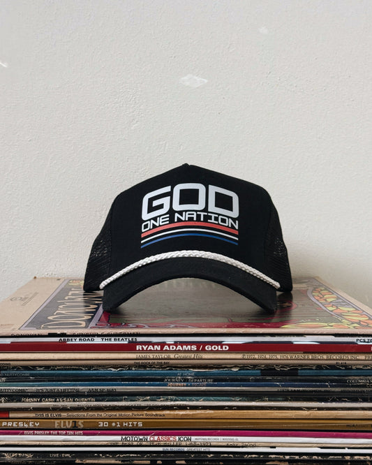 A black baseball cap with white text 'GOD ONE NATION' on the front, placed on a stack of vinyl records.