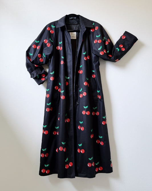 A black trench coat with a pattern of red cherries displayed against a neutral background.